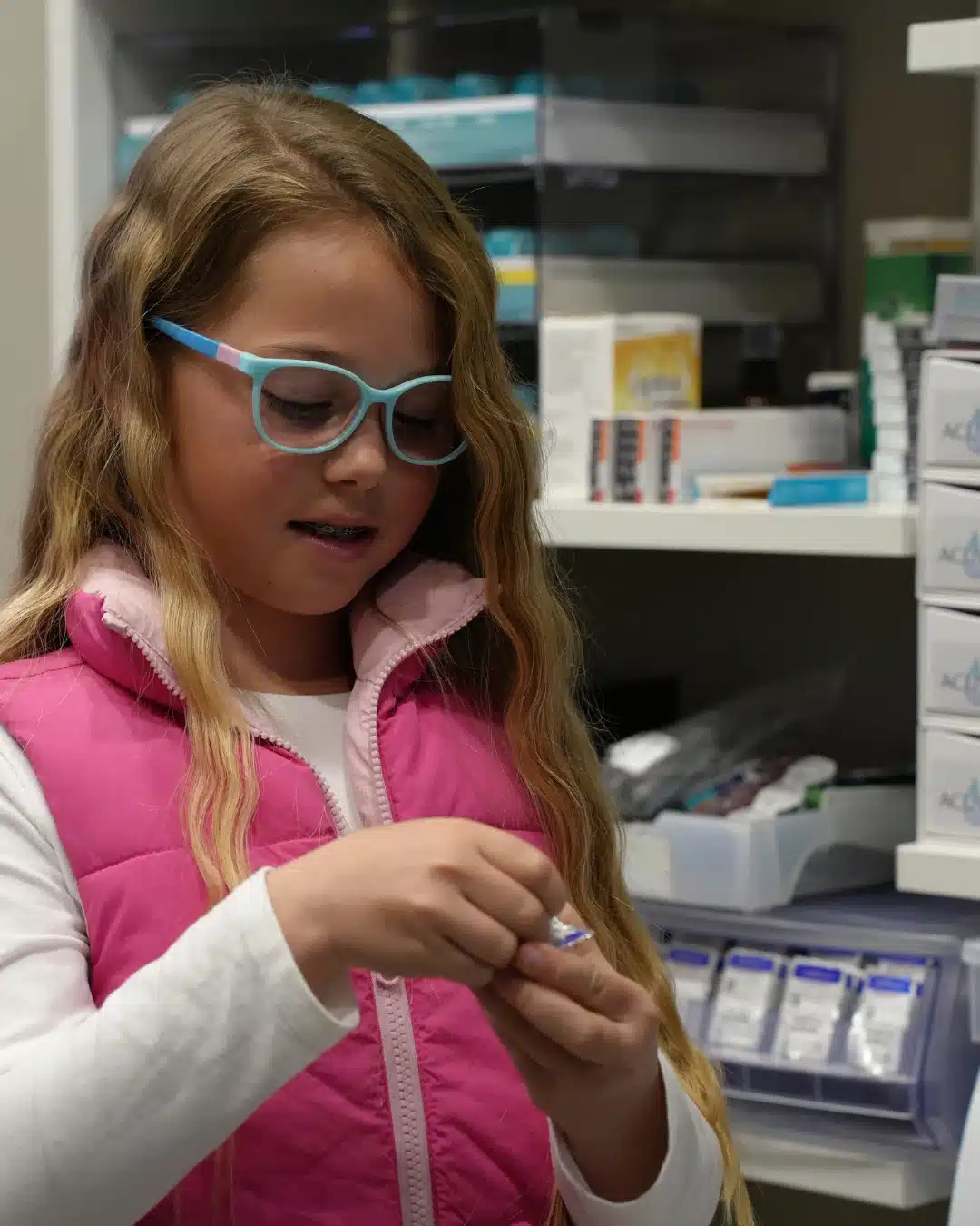 Young patient in spectacles inspecting a contact lens beside a display of contact lens products at Reza Ferreira Optometrist